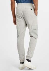 Grå joggebukser med en smal passform, som har cargo-lommer på sidene og ribbet mansjetter. Sammen med hvite joggesko.