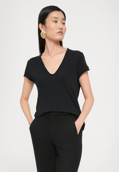 Top nero a maniche corte con scollo a V in un tessuto morbido. Abbinato a pantaloni neri su misura con dettagli in bottone laterali. Design semplice e minimalista.
