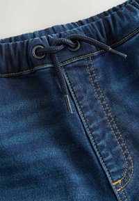 Tumedate denim lühikesed püksid elastse vöökohaga, nööriga ja kollase õmblusega õmbluste ümber. Tekstuuriga kangapind.