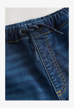 Temno modri denim kratki hlače z elastičnim pasom, s sivko in rumenim šivom vzdolž šivov. Teksturna površina tkanine.