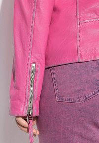 Rosa Lederjacke mit einem Reißverschluss an den Ärmelbündchen, mit glatter Textur und silbernem Zubehör. Getragen über passendem lila Denim.