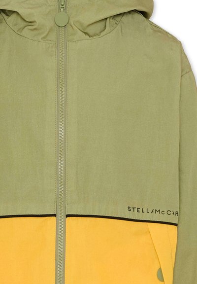 Zielona i żółta kurtka z kapturem zapinana na zamek z przodu, o prostym kroju z kontrastowymi czarnymi przeszyciami. W widocznym miejscu logo marki.