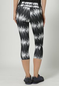 Czarno-białe leginsy capri w wzory o dopasowanym kroju i szerokim pasie, ukazujące teksturowany materiał oraz odblaskowe akcenty.