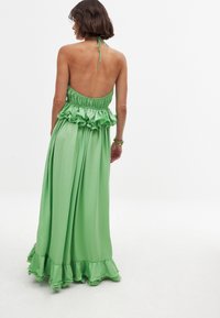 Vihreä naruolkainen mekko, joka on valmistettu virtaavasta kankaasta. Mekossa on kootut vartalo-osa ja röyhelöinen helma. Pehmeä tekstuuri ja pitkä, löysä siluetti.