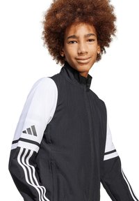 Zwart-witte ritssluitingjas met verticale strepen en het Adidas-logo op de mouwen, gemaakt van lichtgewicht materiaal, met een opstaande kraag.
