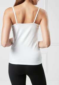 Top alb ajustat cu bretele subțiri, textură netedă și design cu spate decupat, purtat cu colanți negri. Stil simplu și minimalist.