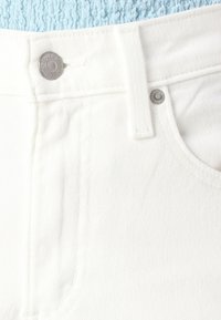 Close-up of white denim jeans waistband with metal button and rivet details against a blue textured fabric background.