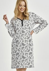 Biała koszula nocna z długim rękawem, ozdobiona czarnym wzorem paisley. Ma dekolt w kształcie litery V z kontrastującą czarną lamówką.