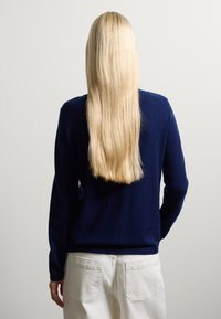 Pull bleu marine à manches longues en matière douce, avec un col rond et une coupe décontractée, associé à un pantalon de couleur claire.