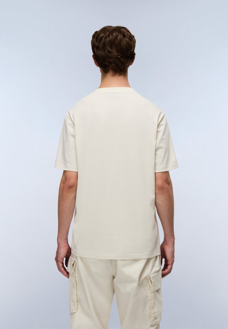 Beige kortærmet t-shirt i blød bomuld med en afslappet pasform. Ryggen har en rund halsudskæring og en jævn tekstur, kombineret med lyse bukser.