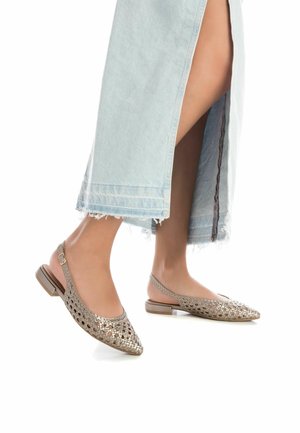 Zapatos planos tipo slingback en dorado metálico, con un diseño trenzado, punta afilada, tacón bajo y parte trasera abierta.