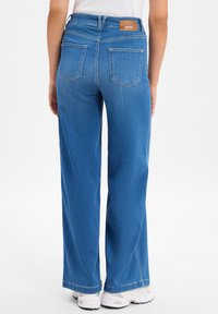 Szerokie niebieskie dżinsy z denimu, z wysokim paskiem, dwiema tylnymi kieszeniami i brązową metką marki na pasku.