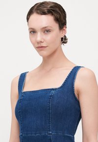 Denim šaty so štvorcovým výstrihom, úzkymi popruhmi a priliehavým tielkom. Majú viditeľné stehy a stredne modrý umývanie.