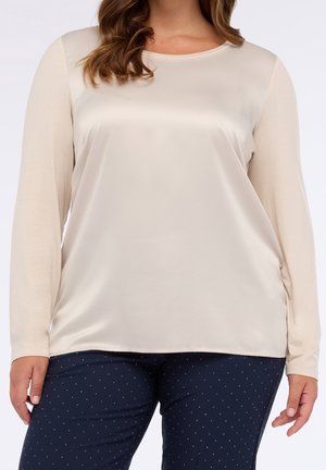 Kobieta ubrana w kremową, długorękawową satynową bluzkę w połączeniu z granatowymi spodniami w drobny biały wzór w groszki.