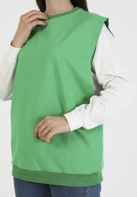 Zielony top z bawełny z luźnym krojem, z krótkimi rękawami typu kimono, okrągłym dekoltem oraz białymi długimi rękawami pod spodem.