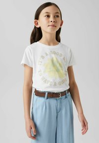Hvid t-shirt med en falmet gul blomst grafik og teksten "Det er en god dag til at have en god dag." Parret med lyseblå bukser og et brunt bælte.