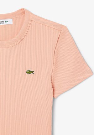 Short-sleeve ribbed t-shirt in soft peach with a round neckline and a small green Lacoste crocodile logo on the chest.