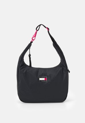 Czarna nylonowa torba na ramię z regulowanym paskiem i różowymi plastikowymi zapięciami, z prostokątną naszywką z logo Tommy Jeans w kolorach czerwonym, białym i niebieskim.