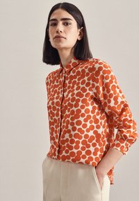 Camicia button-up con una base color crema e audaci pois rossi irregolari. Maniche lunghe con polsini e colletto classico. Tessuto morbido al tatto.
