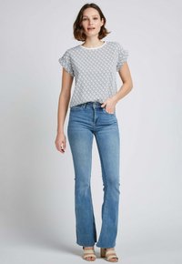 Haut à manches courtes blanc avec un motif géométrique noir, associé à un jean évasé bleu clair et des sandales à plateforme beiges.