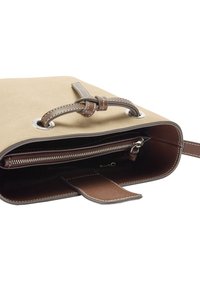 Beżowa torba z zamszu z brązowym skórzanym sznureczkiem oraz wewnętrzną kieszenią na zamek błyskawiczny, otwarta, aby pokazać wykończenie wnętrza i szczegóły komór.