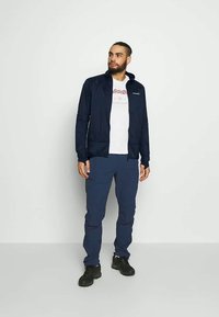 Navy blue lightweight jacket, fitted design with a hood, paired with navy pants and black footwear. Features a white graphic t-shirt underneath.