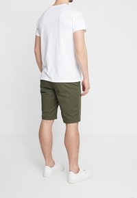 Biała koszulka z krótkim rękawem, oliwkowe szorty i białe tenisówki. Szorty mają prosty krój i kieszenie.