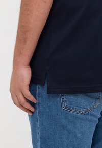 T-shirt in cotone blu navy con spacchi laterali, maniche corte e orlo dritto. Indossato con jeans in denim blu con tasca sul retro.