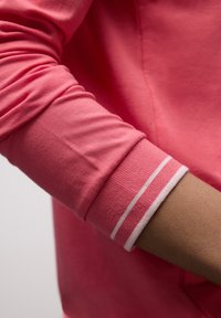 Chemise à manches longues rose avec poignets côtelés ornés de doubles rayures blanches. Matière en coton doux, texture lisse avec une légère brillance.