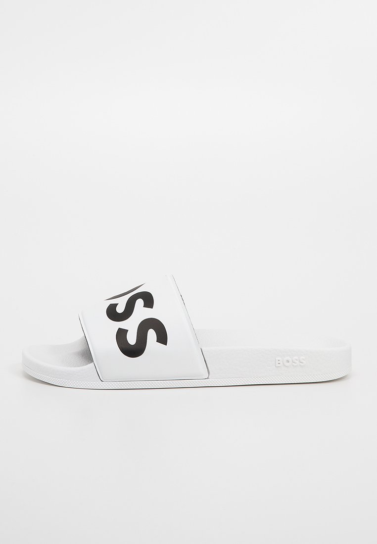 Sandale glissante synthétique blanche avec une large sangle présentant un logo "BOSS" noir. Semelle intérieure texturée et semelle en caoutchouc plate conçue pour le confort.