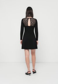 Black long-sleeve dress with a lace back detail and adjustable neckline opening, featuring a flared skirt and fitted bodice.