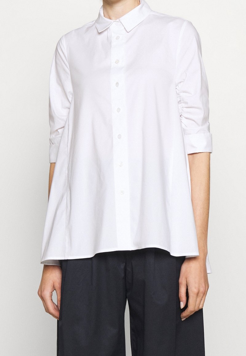 Camicia bianca con colletto a punta, maniche a tre quarti e taglio morbido. Tessuto in cotone morbido con una leggera trama e senza fantasie.