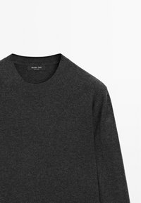 Pull gris foncé à col rond en tissu doux avec manches longues, montrant la partie supérieure avant et la zone du cou avec une étiquette de marque visible à l'intérieur du col.