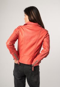 Rode leren jack met een aansluitend ontwerp, ritsmanchetten en stikseldetails. Draagt u met zwarte denim broek, wat een hedendaagse stijl accentueert.