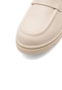Béžové kožené mokasíny s okrúhlym špičkou, kontrastným prešívaním a textúrovanou podrážkou. Majú hladký vrch a minimalistický dizajn.