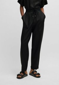 Czarne, lekkie spodnie z elastycznym paskiem na sznurku w talii, kieszeniami po bokach i luźnym krojem; zestawione z prostymi czarnymi sandałami.
