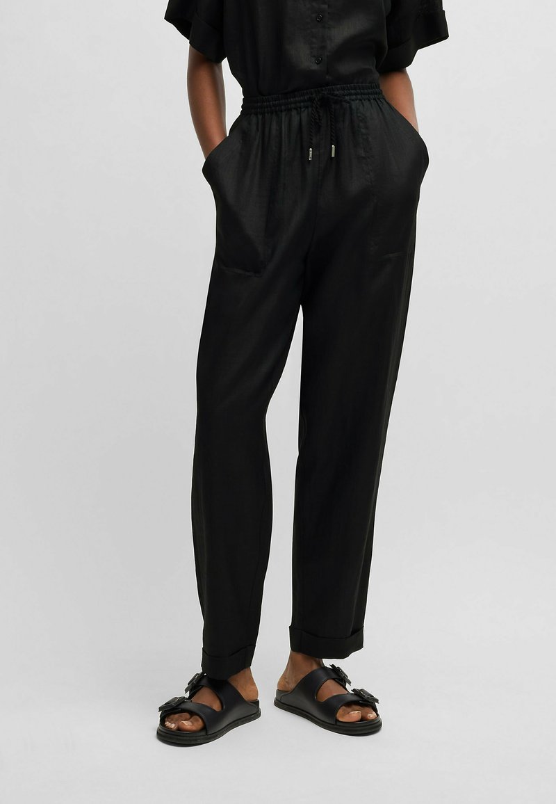 Czarne, lekkie spodnie z elastycznym paskiem na sznurku w talii, kieszeniami po bokach i luźnym krojem; zestawione z prostymi czarnymi sandałami.