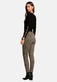 Sweater negro de punto con detalles en corte en las mangas, combinado con pantalones skinny de estampado de leopardo. La modelo lleva botas de tacón negras.
