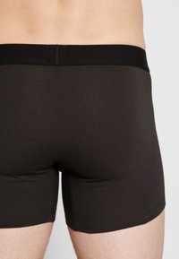 Schwarze Baumwoll-Boxershorts mit glatter Textur, elastischem Bund und kontrastierenden Nähten. Von hinten betrachtet, um die Passform hervorzuheben.