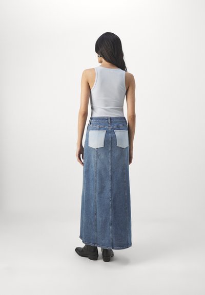 Denim maxi skirt with a high waist, featuring light blue patch pockets, a straight cut, and a medium wash. Paired with a fitted white tank top.