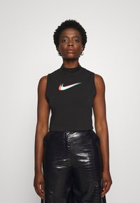Čierny bezrukávový crop top s vysokým golierom, na prednej strane s multicolor logom Nike. Model má na sebe lesklé čierne textúrované nohavice.