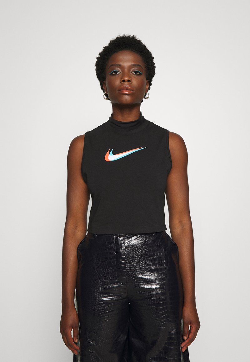 Top corto nero senza maniche con collo alto, caratterizzato da un logo Nike multicolore sul davanti. Il modello indossa pantaloni neri lucidi e testurizzati.