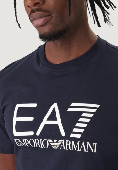 Тъмносин памучен тениска с бяло графично лого с надпис "EA7" и "EMPORIO ARMANI". Класическа кръгла яка с гладка текстура.