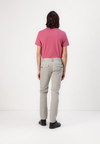 Pantalons gris et T-shirt rose. Les pantalons ont des poches arrière avec boutons ; le tissu semble lisse, avec une coupe ajustée et des jambes droites.