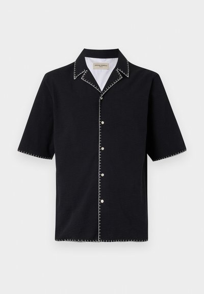 Black short-sleeve shirt with a collar, featuring white contrast stitching along the edges and buttons down the front. Textured fabric.