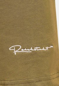 Tessuto verde oliva con una sottile trama a coste, arricchita da dettagli di ricamo bianco con firma. Superficie liscia con un leggero lucido.