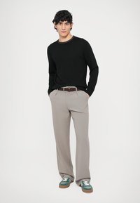 Fekete kötött pulóver, világosszürke csíkos nadrág, barna fonott öv és zöld tornacipő fehér fűzővel. A modell zsebébe tett kézzel áll.