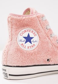Baskets montantes Converse Chuck Taylor All Star rose avec une texture duveteuse et une semelle en caoutchouc blanche, vues de profil.