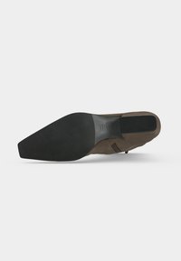 Chaussure habillée en daim marron vue par la semelle avec une semelle extérieure en caoutchouc noir pointu et un talon carré sur fond blanc.