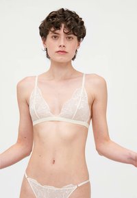 Brassière en dentelle transparente avec broderie florale, bonnets triangulaires et fines bretelles réglables. Accompagnée d'un string en dentelle transparente assorti.